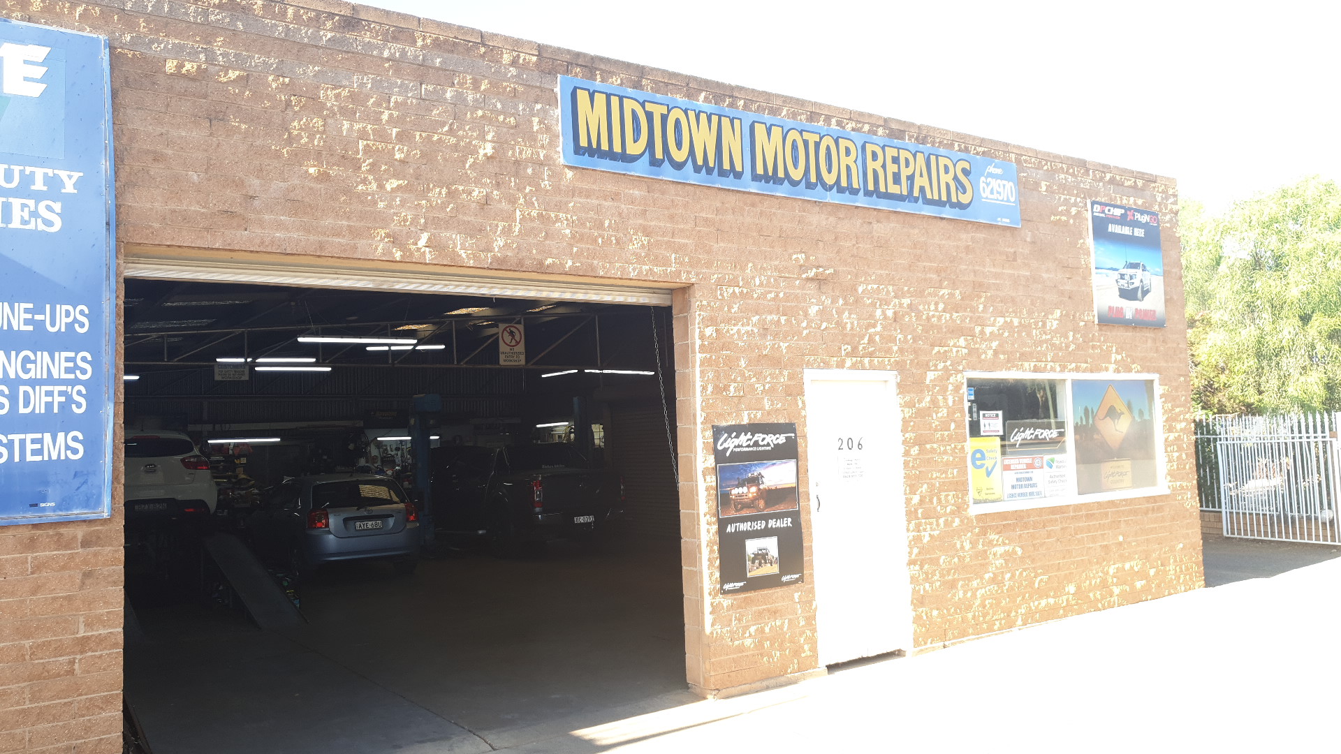Inside the Midtown Motor Repairs workshop with the roller door up and cars on the hoist